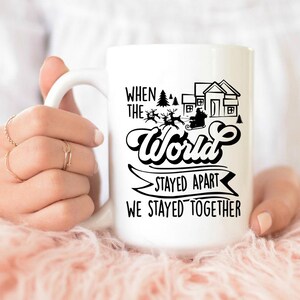 May include: White ceramic coffee mug with a black design that reads "When the world stayed apart we stayed together". The design also includes a silhouette of Santa Claus in a sleigh with reindeer flying over a small town.