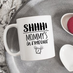 May include: White ceramic coffee mug with black text that reads "SHHH! MOMMY'S in TIMEOUT" and a black and white illustration of an alarm clock.