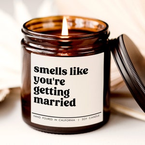 May include: A brown glass candle jar with a white label that reads "smells like you're getting married". The candle is lit and the jar has a black lid.