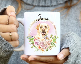 Op de afbeelding: Witte keramische mok met een bloemenontwerp en een gouden cirkel rond een aquarelimage van een gele Labrador Retriever. De naam van de hond, "Juno", is in cursief geschreven boven het hoofd van de hond.