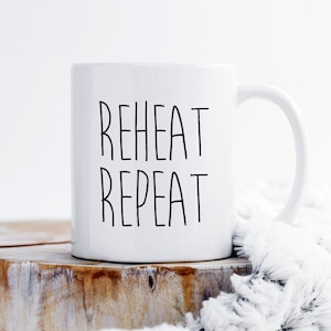 May include: White ceramic coffee mug with black text that reads "REHEAT REPEAT".