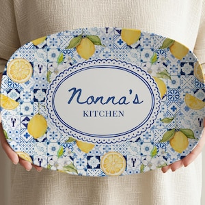 May include: Oval serving platter with a blue and white tile pattern, lemons, and the text "Nonna's Kitchen" in a decorative oval. The platter has a scalloped edge and is held by a person.