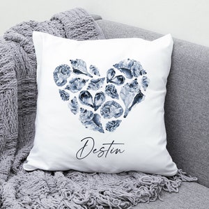 May include: White pillow with a blue watercolor heart design made of seashells. The text "Destin" is written in cursive below the heart.