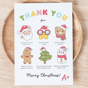 以下が含まれることがあります： カラフルな文字で「THANK YOU」と書かれた白いクリスマスカード。サンタ、アヒル、クマ、ジンジャーブレッドマン、クリスマスツリー、雪だるまの漫画イラストが特徴です。「メリークリスマス！」と「A+」の文字が含まれています。