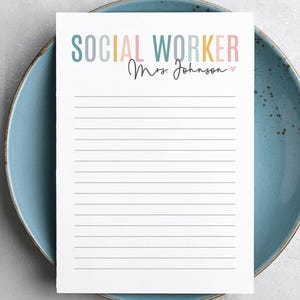 May include: A white notepad with lined paper and the text "SOCIAL WORKER" in rainbow colors. The name "Mrs. Johnson" is written in cursive below the text.