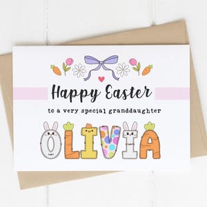 May include: A white card with a pink and white striped banner that says "Happy Easter to a very special granddaughter". The name "Olivia" is spelled out in colorful letters decorated with bunnies, carrots, and eggs.