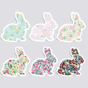 May include: Six colorful bunny rabbit silhouettes with floral patterns. The bunnies are in various colors, including pink, blue, green, and black. Each bunny has a different floral pattern.