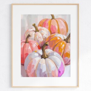 May include: A framed art print featuring a still life of pumpkins. The pumpkins are painted in shades of pink, orange, and white, with green stems. The artwork has a soft, painterly style, perfect for fall decor.