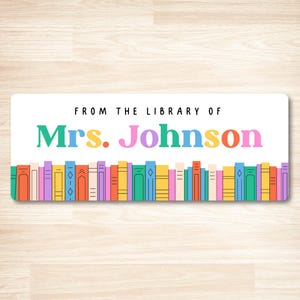 May include: A rectangular sticker with the text "FROM THE LIBRARY OF Mrs. Johnson" in a colorful font. The bottom of the sticker features a row of illustrated books in various colors, including orange, yellow, green, and purple.