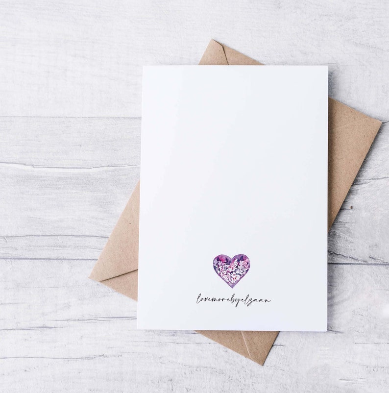 May include: A white card with a purple floral heart and the text "love more, by design". The card is sitting on a brown envelope.