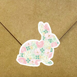 May include: A white sticker with a pink and green floral pattern in the shape of a rabbit. The rabbit is sitting on a brown paper background.