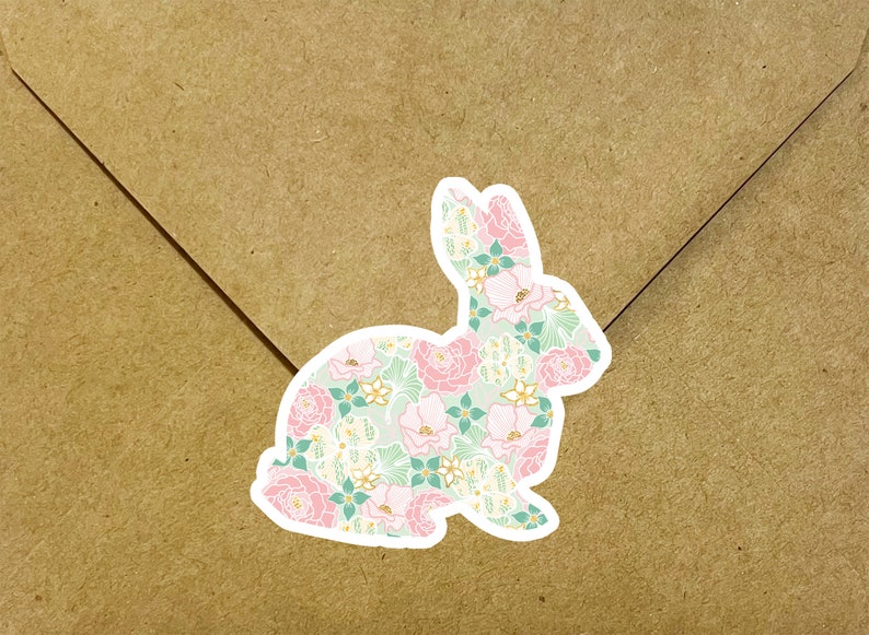 May include: A white sticker with a pink and green floral pattern in the shape of a rabbit. The rabbit is sitting on a brown paper background.
