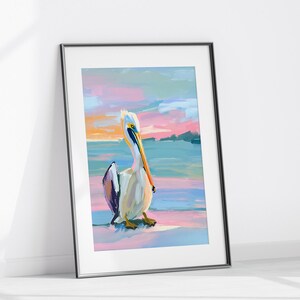 May include: A framed painting depicting a pelican standing on a beach with a colourful sunset in the background. The pelican is white with a long orange beak and black and purple feathers on its wings. The sunset is a mix of pink, orange, and blue.