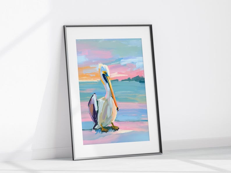 May include: A framed painting depicting a pelican standing on a beach with a colourful sunset in the background. The pelican is white with a long orange beak and black and purple feathers on its wings. The sunset is a mix of pink, orange, and blue.