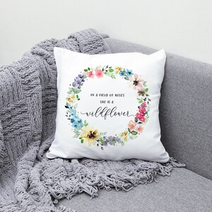 May include: White throw pillow with a watercolor floral wreath and the text "In a field of roses she is a wildflower".