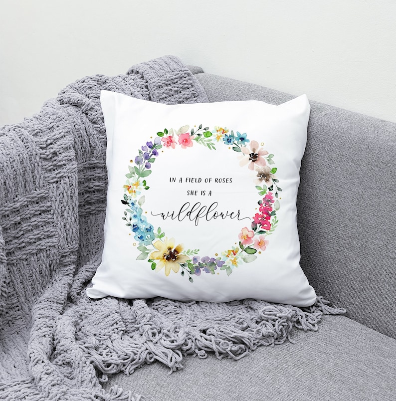 May include: White throw pillow with a watercolor floral wreath and the text "In a field of roses she is a wildflower".