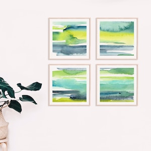 May include: Set of four abstract watercolor paintings in shades of green, blue, and yellow. The paintings are framed in natural wood frames and are arranged in a grid pattern on a white wall.