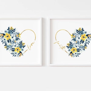 May include: Two framed art prints featuring heart-shaped designs. Each heart is composed of blue and yellow watercolor flowers, with a gold outline. One print says "love" and the other says "faith" in gold script.