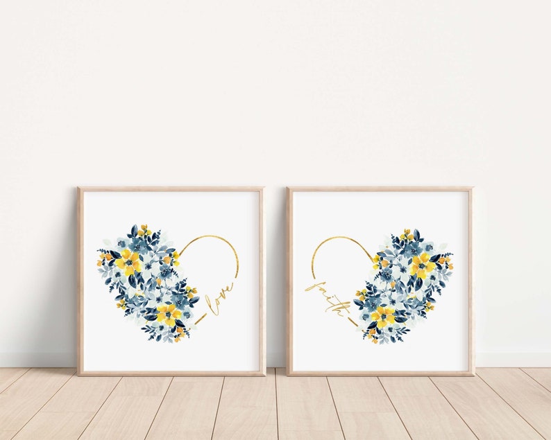 May include: Two framed art prints featuring watercolor floral heart designs. One print says "love" and the other says "faith" in gold script. The floral arrangements include blue and yellow flowers.