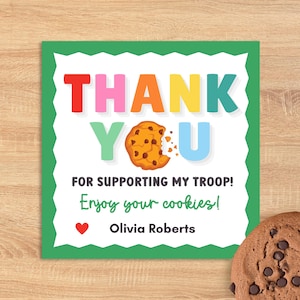 May include: A square card with a green border and a white interior features the words "THANK YOU" in colorful letters. Below, it reads "FOR SUPPORTING MY TROOP! Enjoy your cookies!" with a heart and name. A chocolate chip cookie is in the corner.
