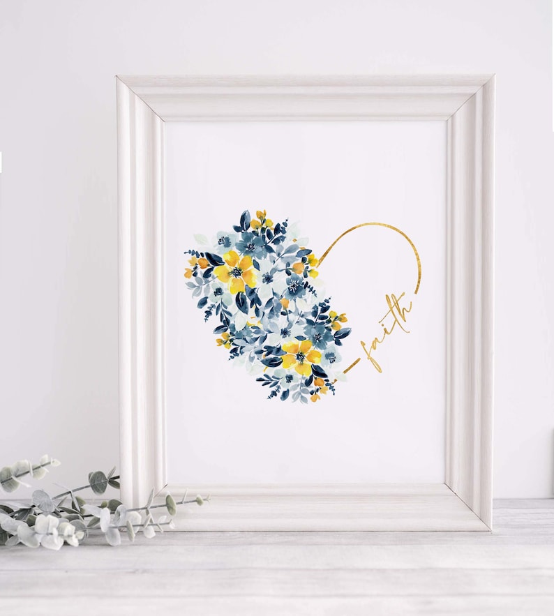 May include: A framed art print featuring a watercolor floral heart design. The heart is composed of blue and yellow flowers. The word "faith" is written in gold script within the heart's outline. The frame is white.