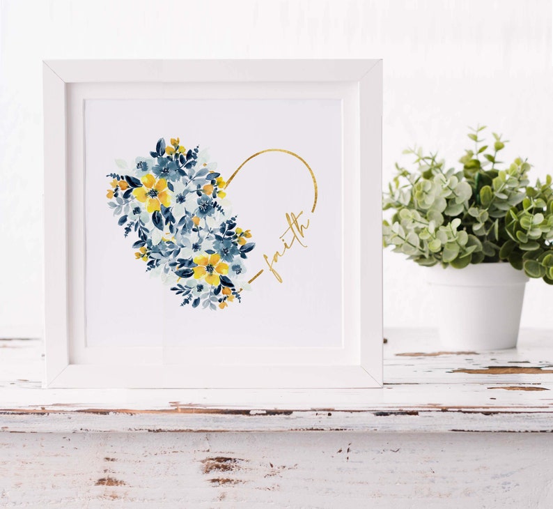 May include: A framed art print featuring a watercolor floral heart design. The heart is composed of blue and yellow flowers, with a gold outline and the word "faith" in gold script. The frame is white.