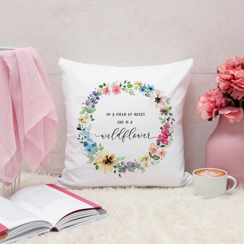 May include: White throw pillow with a watercolor floral wreath and the text "In a field of roses she is a wildflower".