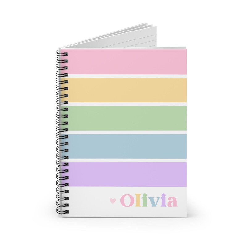 Op de afbeelding: Een spiraalgebonden notitieboek met een pastelkleurige regenboog gestreepte omslag. Het notitieboek heeft roze, gele, groene, blauwe en paarse strepen. De naam "Olivia" is in pastelkleuren gedrukt met een klein hartje.