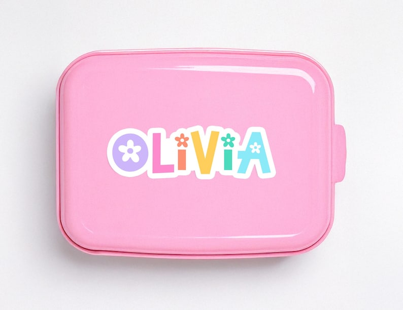 May include: A pink lunchbox with rounded edges. The word "Olivia" is printed on the front in colorful letters, each with a flower accent. The lunchbox has a handle on the side.