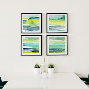 May include: Four framed abstract watercolor paintings in shades of green, blue, and yellow. The paintings are arranged in a grid pattern on a white wall.