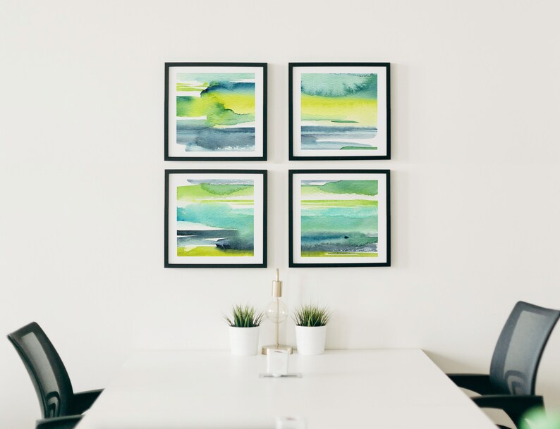 May include: Four framed abstract watercolor paintings in shades of green, blue, and yellow. The paintings are arranged in a grid pattern on a white wall.