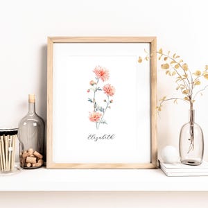 May include: A framed floral print featuring watercolor-style peach-colored flowers with green stems and leaves. The name "Elizabeth" is written in cursive below the flowers. The frame is light wood. A glass bottle, corks, and matches are on the shelf.