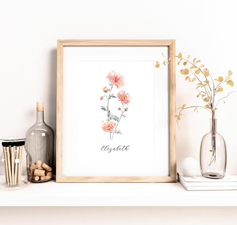 May include: A framed floral print featuring watercolor-style peach-colored flowers with green stems and leaves. The name "Elizabeth" is written in cursive below the flowers. The frame is light wood. A glass bottle, corks, and matches are on the shelf.