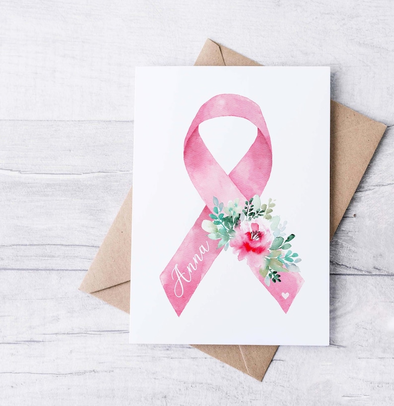May include: Watercolor illustration of a pink ribbon with the name "Anna" and floral accents. The ribbon is a symbol of breast cancer awareness. The card is on a white background with a brown envelope.