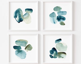 May include: Four framed abstract watercolor prints. Each square frame contains a unique arrangement of blue, teal, and beige organic shapes. The artwork has a minimalist style, with soft edges and a calming aesthetic, suitable for home decor.