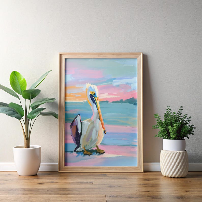 May include: A framed painting of a pelican standing on a beach with a pink and blue sunset in the background.