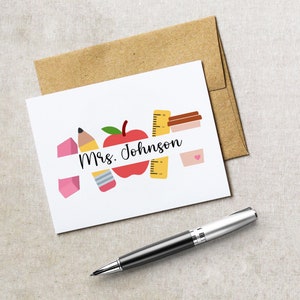 May include: A white card with a red apple, yellow ruler, pink eraser, and a pencil. The text "Mrs. Johnson" is written on a white banner.