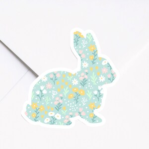 May include: A light blue bunny silhouette sticker with a floral pattern. The pattern includes white, pink, yellow, and green flowers on a light blue background.