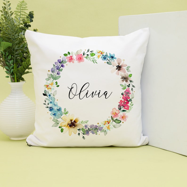 May include: White pillow with a floral wreath design and the name "Olivia" in black script.