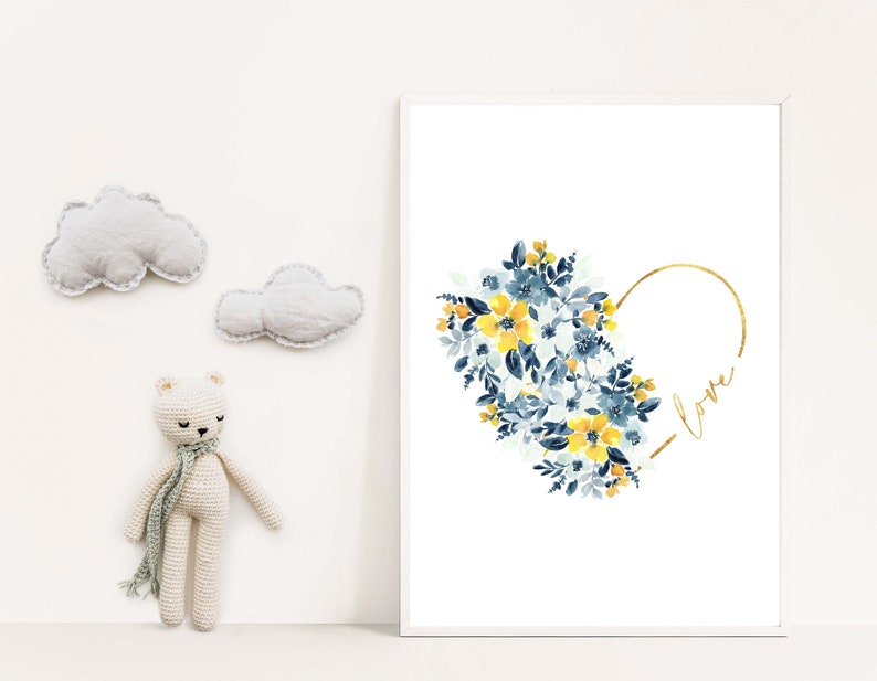 May include: A framed art print featuring a watercolor floral heart design in yellow and blue, with the word "love" in gold script. Decorative clouds and a crocheted bear are also in the image.