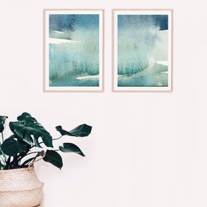 May include: Two framed abstract watercolour paintings in shades of blue and green. The paintings are hung on a white wall.