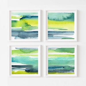 May include: Set of four abstract watercolor paintings in shades of green, blue, and yellow. The paintings are framed in white and hung on a white wall.