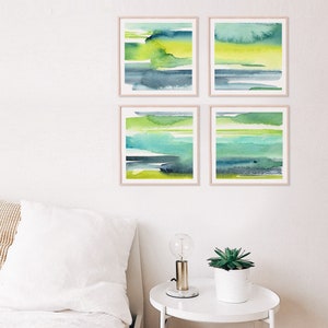 May include: Set of four abstract watercolor paintings in shades of green, blue, and yellow. The paintings are framed in a light wood frame and are hung on a white wall.