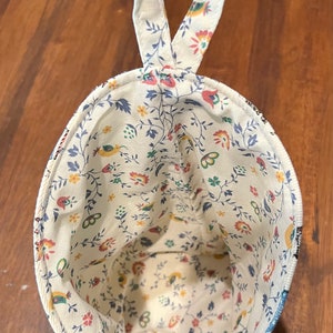 May include: A white fabric hanging storage organizer with a floral pattern in shades of blue, red, yellow, and green. The organizer has a loop handle at the top.