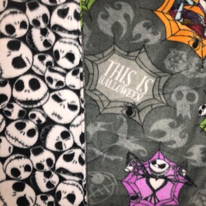 May include: A fleece blanket featuring a patchwork design. One side displays a pattern of Jack Skellington faces in black and white. The other side has a gray background with spiderwebs, skulls, and the text "THIS IS HALLOWEEN".