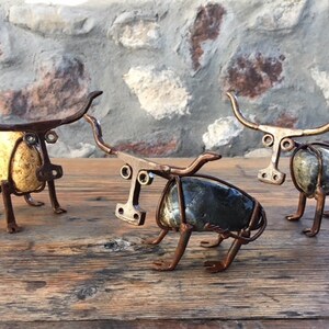 May include: Three metal sculptures of bulls, each with a different coloured stone for a body. The bulls are made of wire and metal scraps and have a rustic, industrial look.