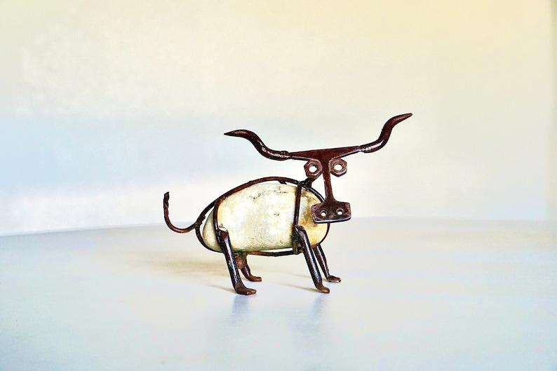 May include: A small, whimsical sculpture of a bull made from metal and a white rock. The bull has long horns, a simple face, and a rounded body.