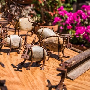 May include: A collection of rustic metal and stone sculptures of stylised bulls. The sculptures are arranged on a wooden surface with a metal bar in the background.