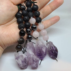 May include: Four crystal pendants with black lava beads, hematite beads, and rose quartz beads. The pendants are made of amethyst and are in the shape of a point. The pendants are strung on black cords.