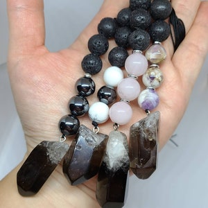 May include: A necklace featuring black lava rock beads, hematite beads, white howlite beads, rose quartz beads, amethyst beads, and four smoky quartz crystal points.